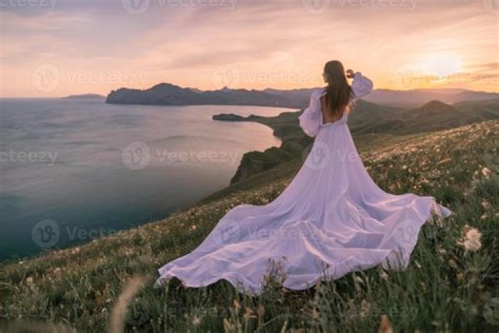 a woman in a long dress standing on the floor with her hands up to her face