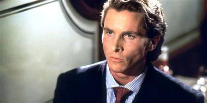 Christian Bale as Patrick Bateman using a huge 80s cellphone wearing glasses and removing a chemical peel from his face in American Psycho