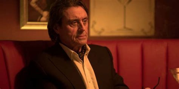 Ian McShane as Winston sitting in a booth in The Continental in John Wick 2