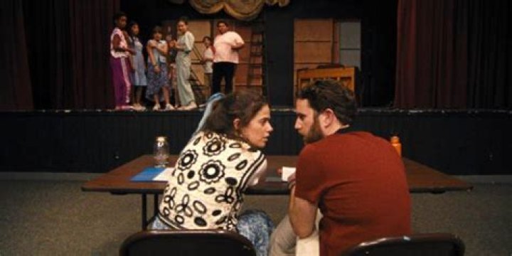 Theater Camp: Angelo and Rebecca talking at a table about the kids on stage&nbsp;